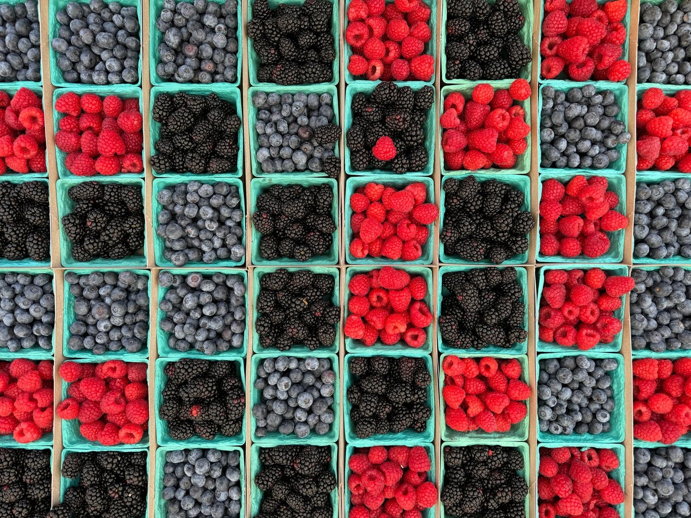 Overhead grid of berry baskets alternating blueberries, raspberries and blackberries