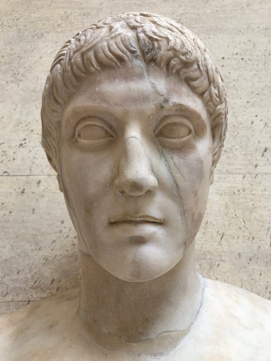 Close-up of a marble portrait head with short curled hair against pale stone