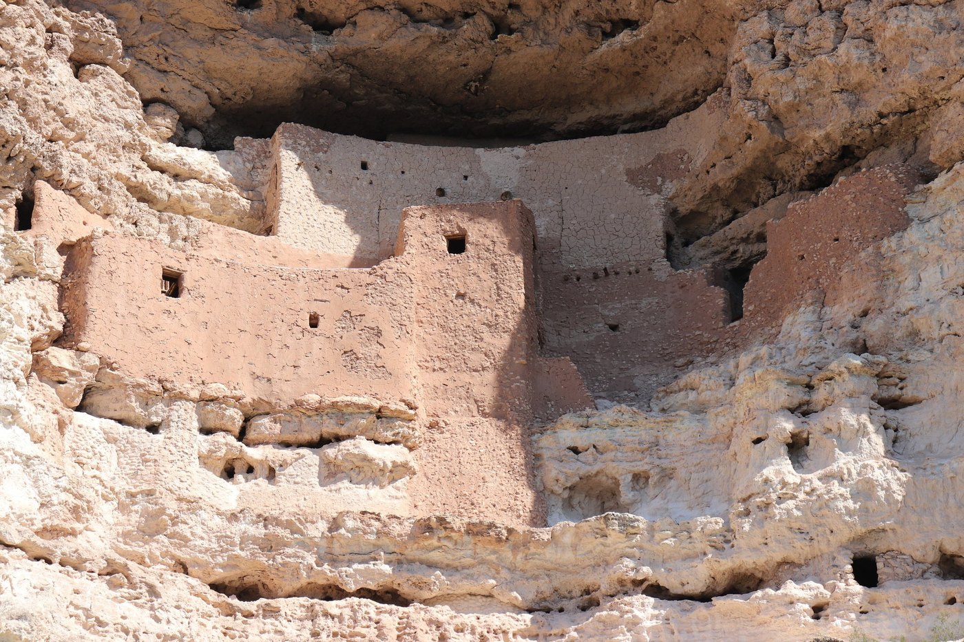 Ancient multi-story adobe cliff dwelling tucked into a pale limestone alcove