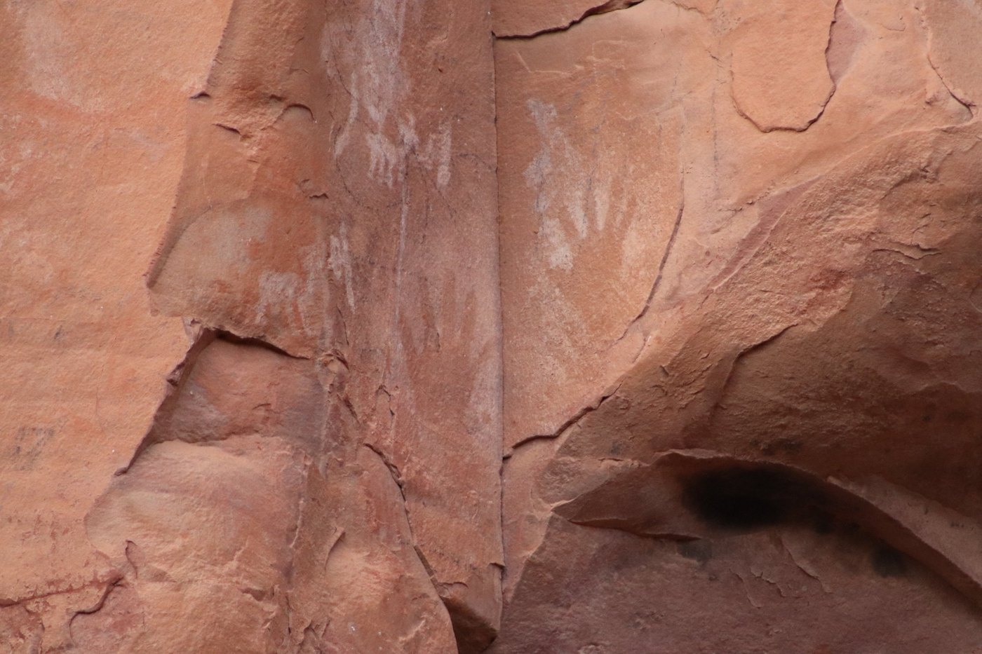 Faint white painted handprints on a smooth, fractured red sandstone wall