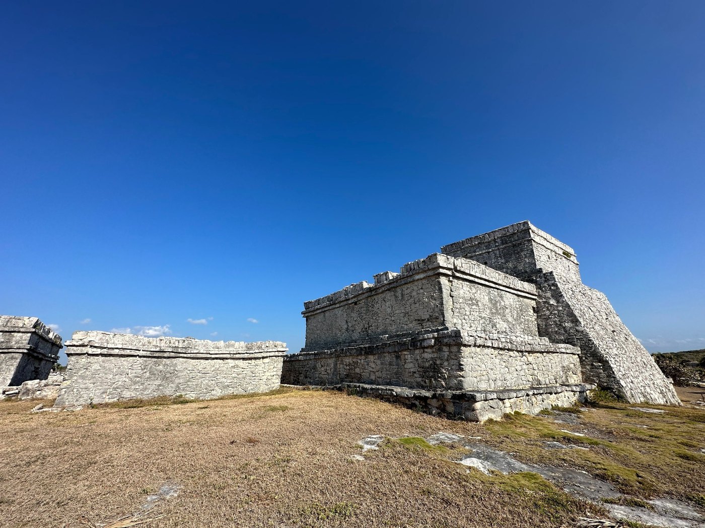 Weathered stone temple ruins on dry grass under a deep blue sky