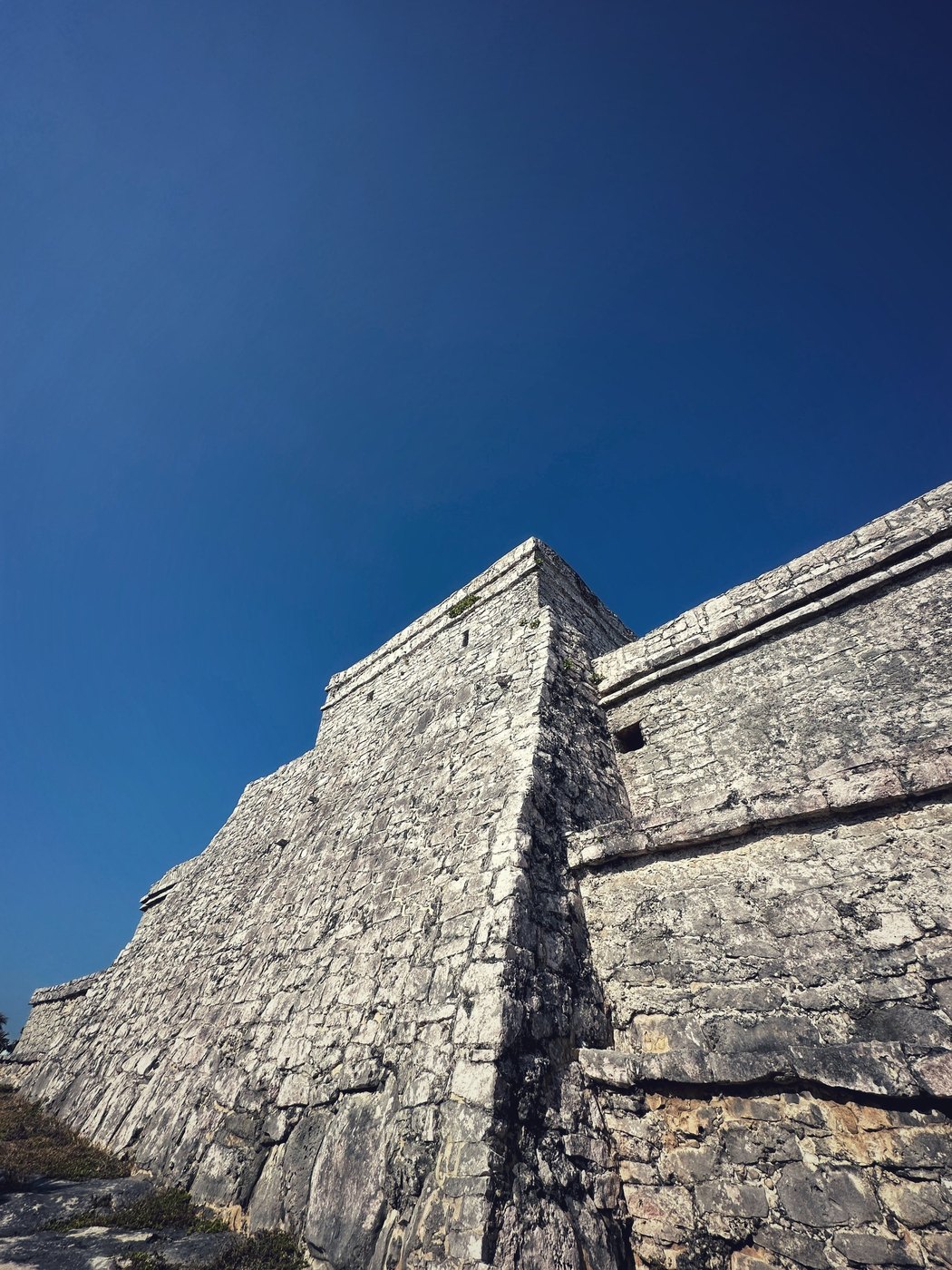 Low-angle view of a sloping stone temple wall rising into a deep blue sky