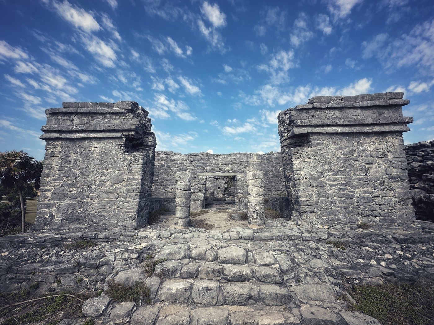 Two weathered stone pillars framing a ruined doorway beneath wispy clouds and blue sky