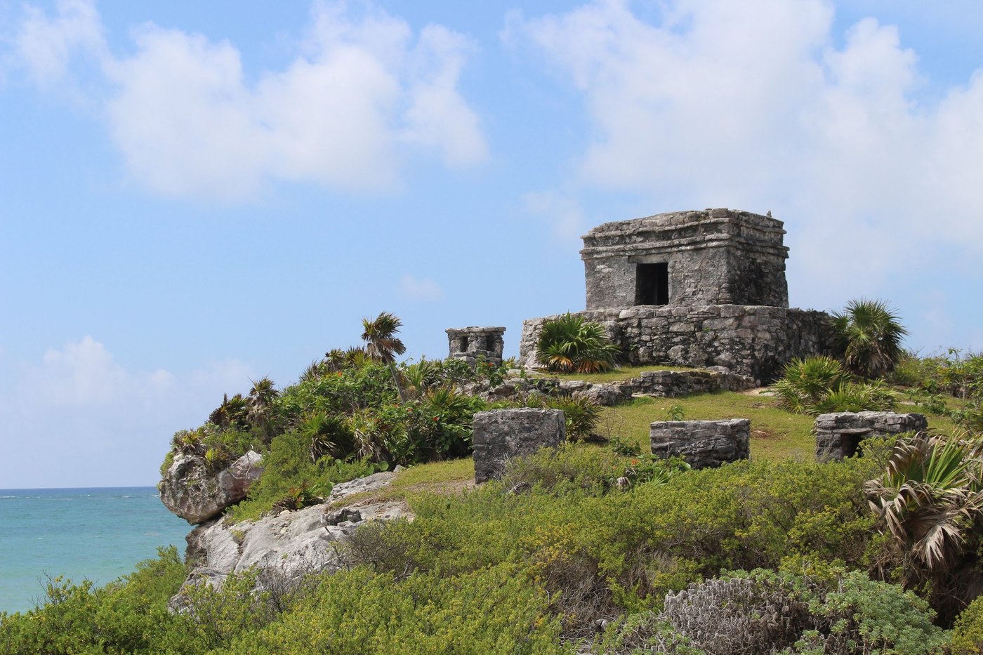 Small stone ruin atop a green grassy bluff above turquoise sea under white clouds