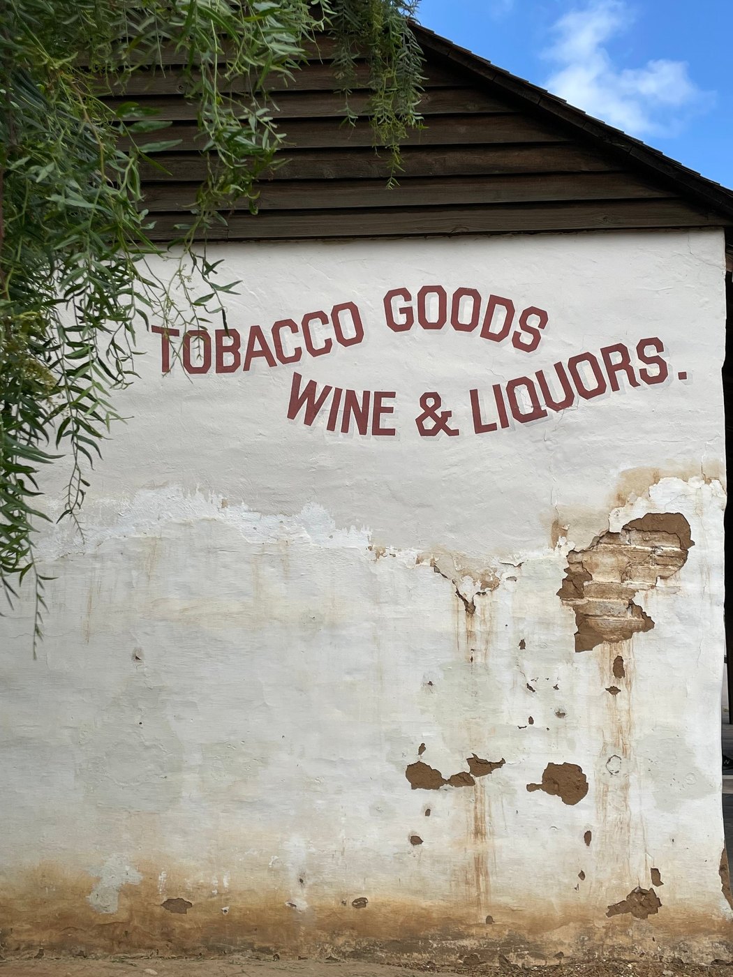 Painted lettering on a weathered white plaster wall with peeling patches under a wooden eave