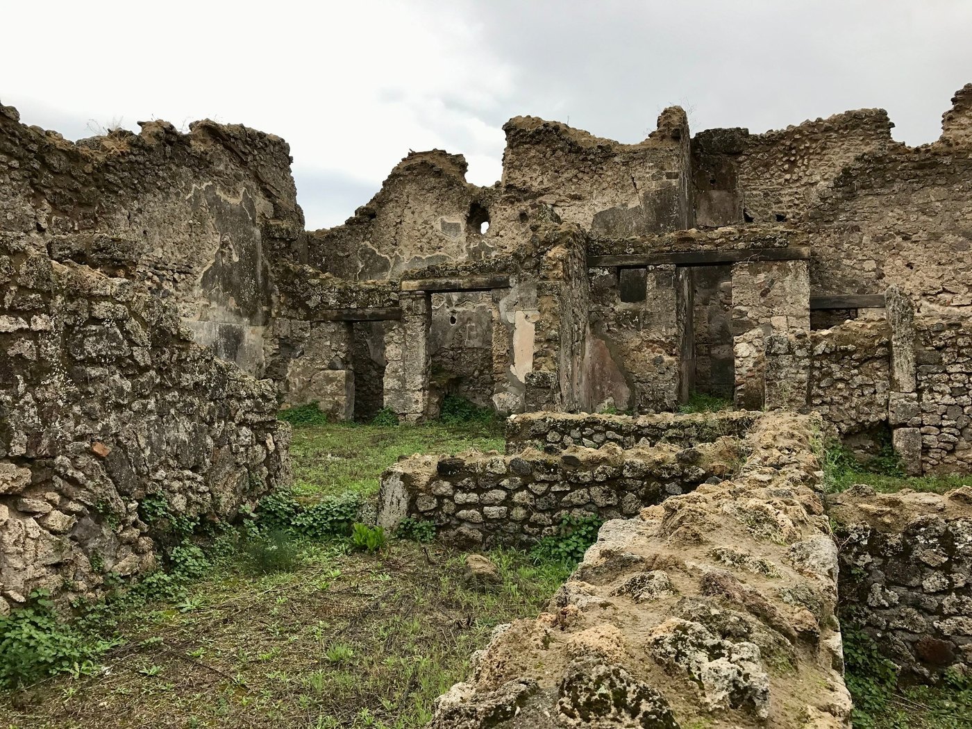 Roofless crumbling stone walls and doorways of ancient ruins under an overcast sky