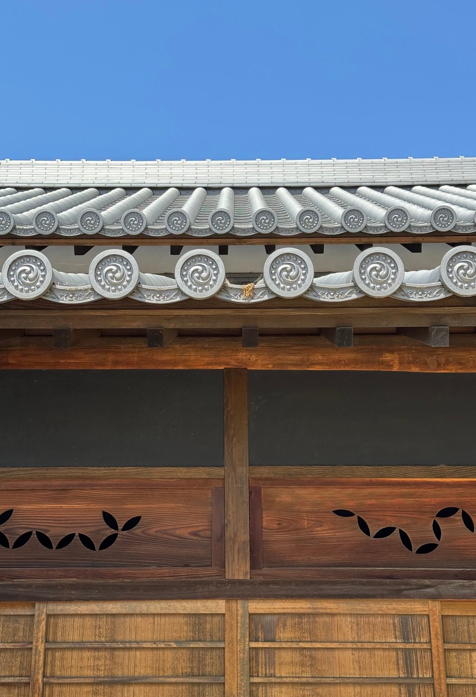Gray tiled roof edge with round decorative end tiles above a dark wooden facade