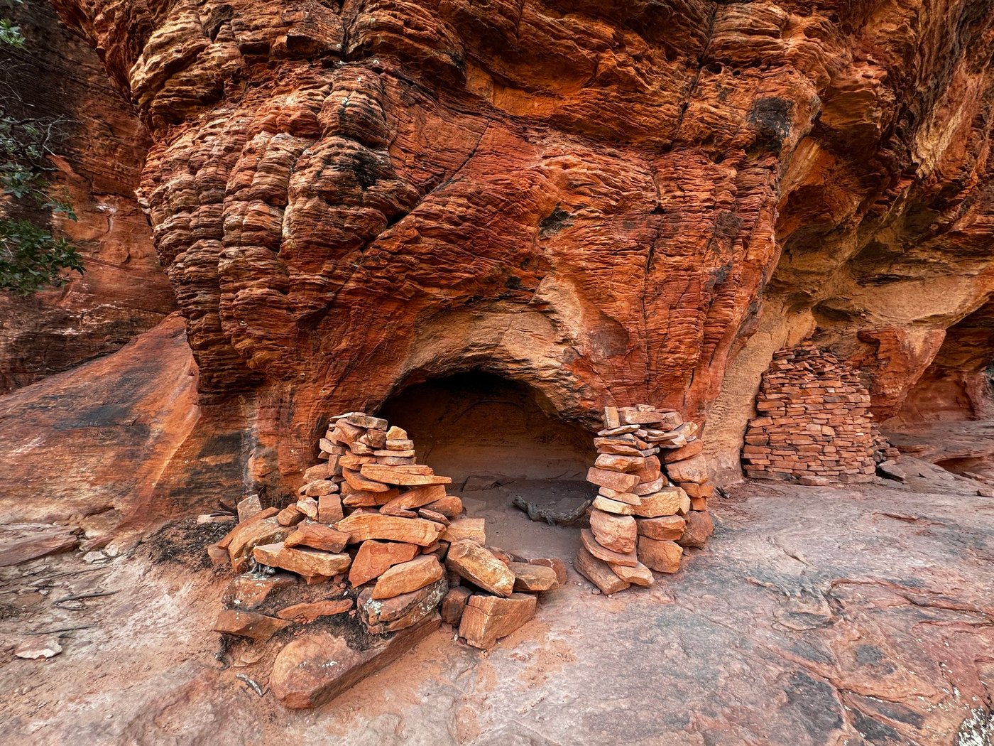 Rippled red sandstone overhang above a small alcove framed by stacked flat stones