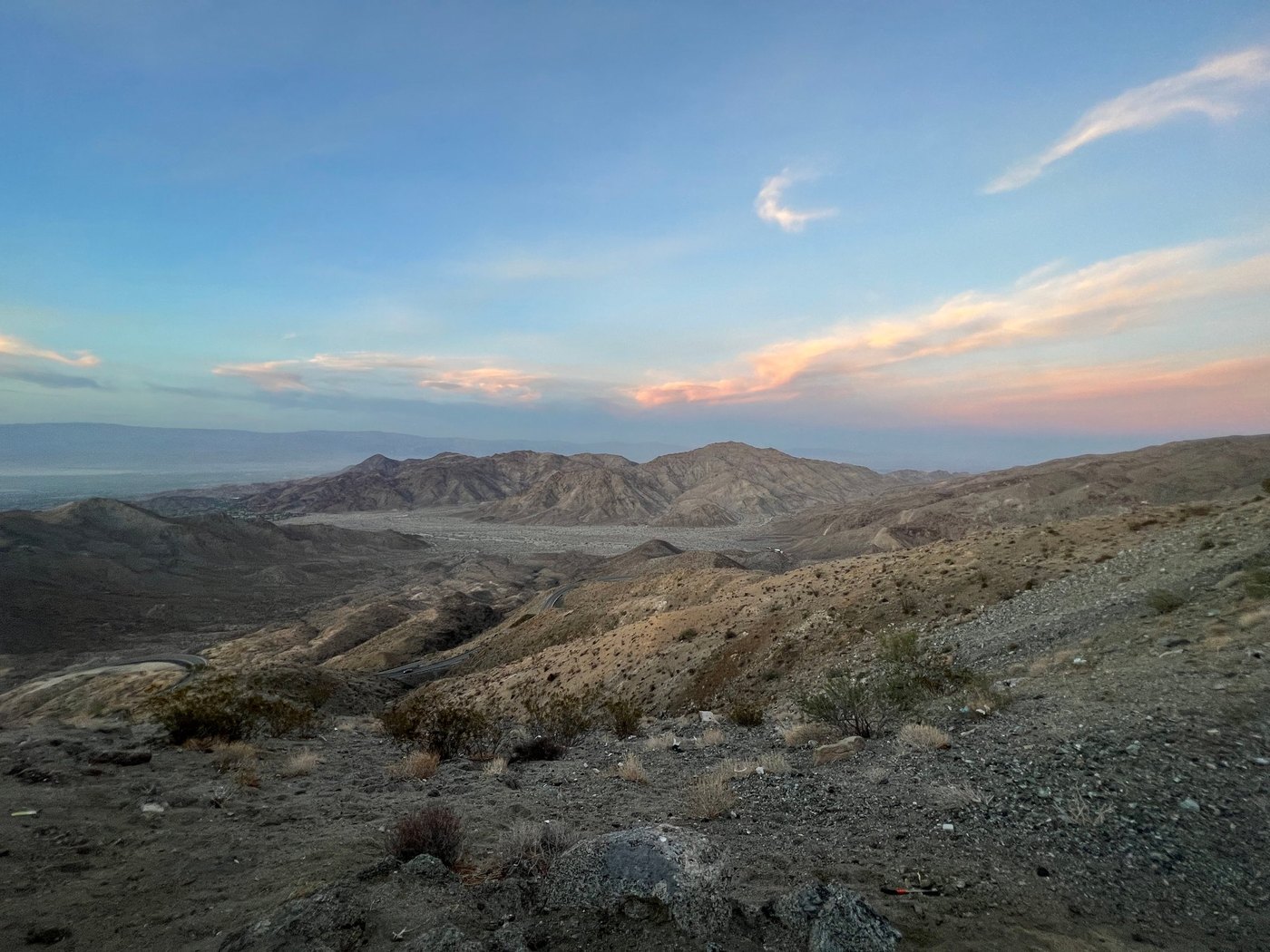 Rugged desert hills and rocky slope at dusk under pale sky with pink-tinged clouds