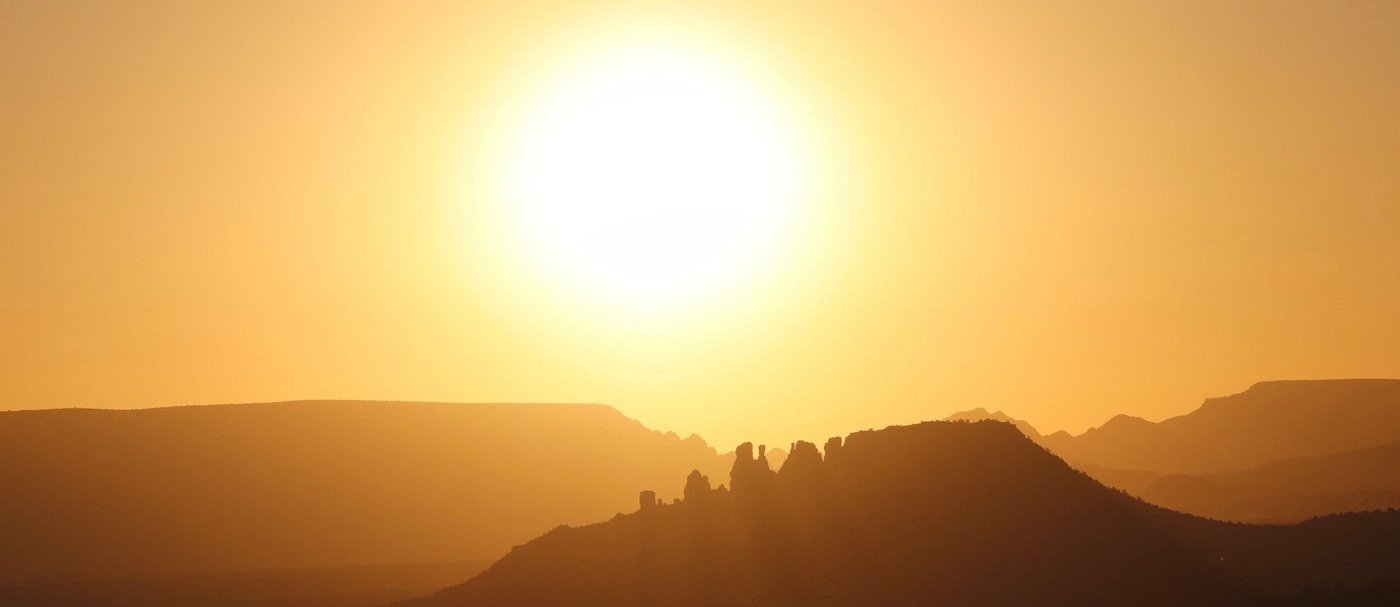 Sun glowing in a hazy amber sky above silhouetted mesas and rock spires